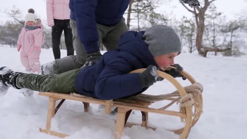Father Launches Son Pushing Sled Down the Hill on Snowy Winter Day in Park Boy Sledge Outdoors Happy