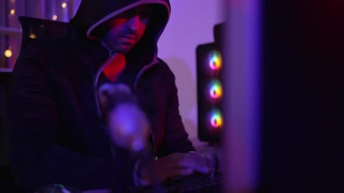 Hooded Person Typing on Computer Keyboard at Night