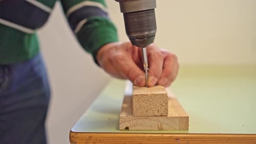 Close-up of a male worker’s hands driving a screw into wood with a cordless drill