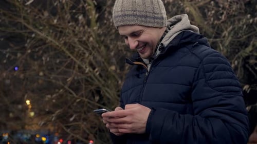 Close up portrait of excited smiley young man texting on smartphone outdoor
