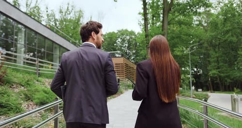 Back View of Businessman and Businesswoman Walking Together Along City Street Near Modern Office