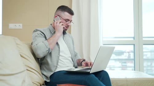 Young Adult Working on Laptop and Talking on Phone