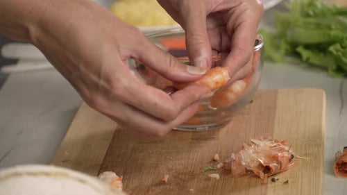 Hands of young woman european takes boiled shrimps and peele them to prepare salad, left side view