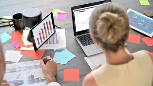 A woman and a man working and talking in the office. Gadgets and papers with graphs and information