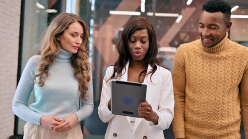 Multiracial group of workers walking in an office and discussing business affairs using a tablet. Sl