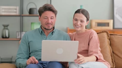 Couple Sitting on Couch Looking at a Laptop