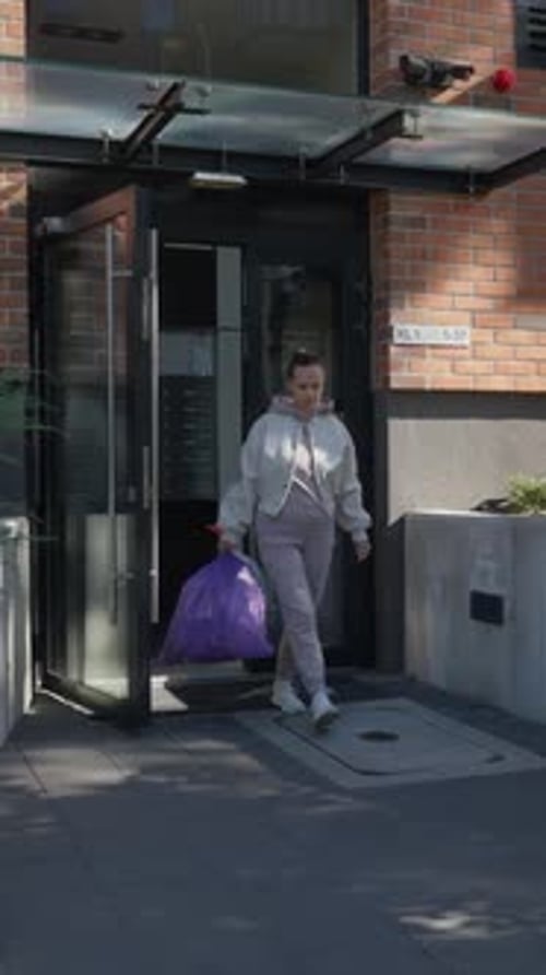 Uma mulher saindo de seu moderno prédio de apartamentos para tirar o lixo