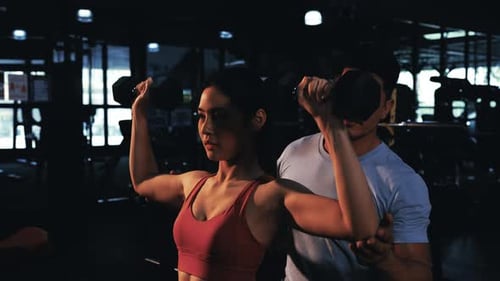Woman Lifts Weights with Help of Personal Trainer