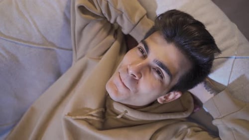 Happy young man lying on sofa. Thoughtful positive teenager.