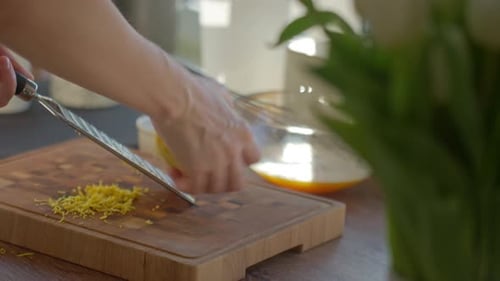 Grating Lemon Zest with Metal Grater on Wooden Cutting Board