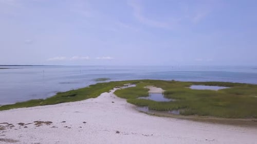 The camera pans from left to right in front of the dune grass, and tidal pools. A kayaker can be see