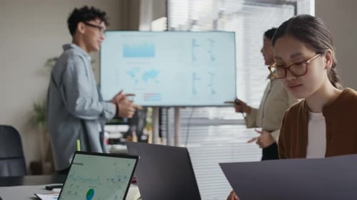 Colleagues Analyzing Chart while Asian Businesswoman Examining Paper in Office
