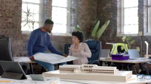 Diverse architect colleagues discussing work with building model and blueprint in slow motion
