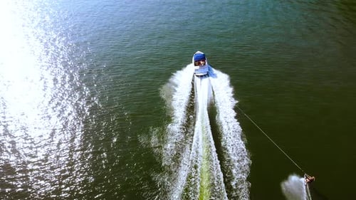Aerial drone footage of tourist enjoying water skiing, tied behind high speed motor boat.