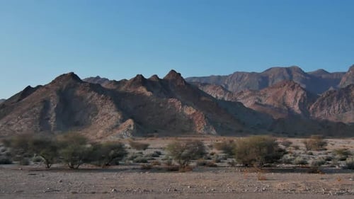 Rugged dry hills and sharp peaks of the Omani desert landscape lit by the afternoon sun travelling s