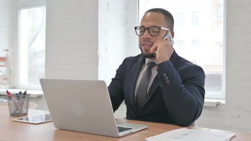 Man in Suit Working on Laptop and Talking on Phone