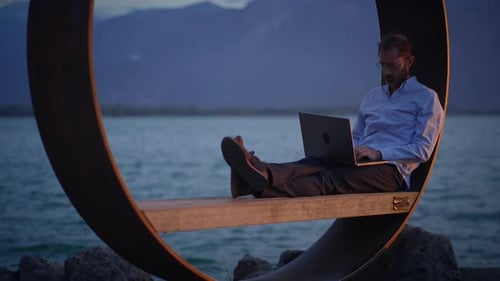 A Man is Working Diligently on His Laptop While Enjoying a Distinctive Coastal Setting