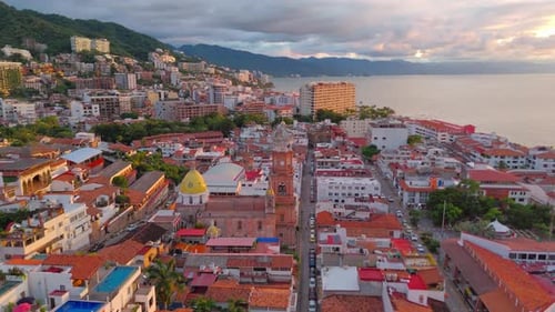 Aerial drone footage of Puerto Vallarta’s iconic church at sunset, with the orange glow of the golde