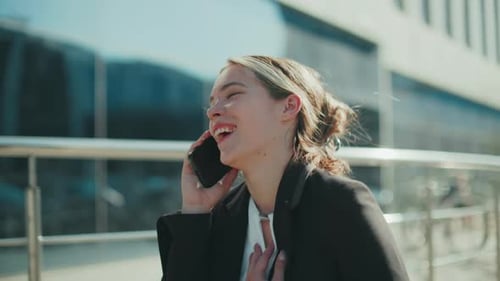 Cheerful Businesswoman Smiling During Phone Call Walking Toward Office Building