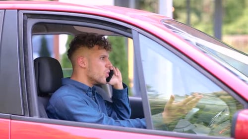 Young Man Sitting in the Car While Talking on the Smartphone Cursing and Nervous Right Hand Drive