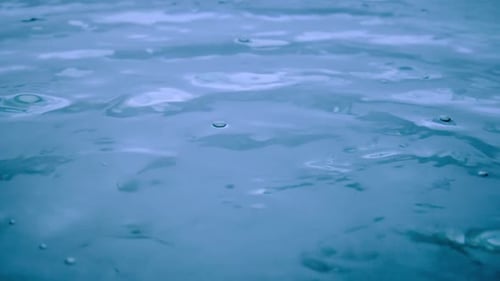 Splash of Water Falling on a Blue Liquid Surface Forming Splashes and Waves