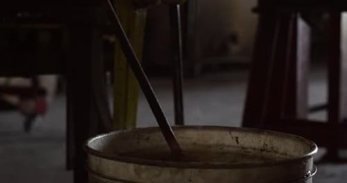 Blacksmith cools red hot iron rod in water creating steam in his workshop