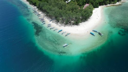 Tilt up shot to a topical island paradise in a blue ocean with white sand and boats at the shore. Ho
