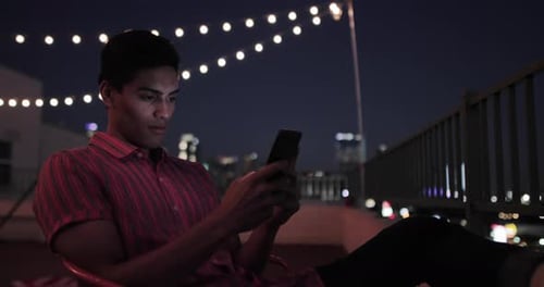 Young Man Using Phone on Rooftop at Night