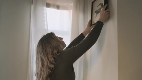 Woman Hanging Picture Frame on Wall Indoors