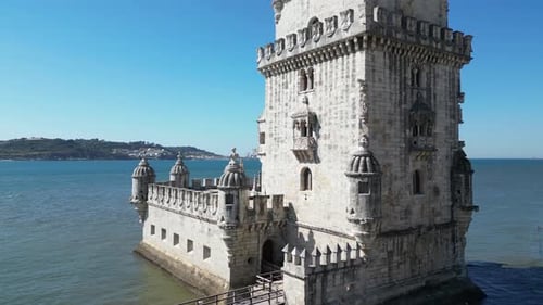 Low aerial orbits base of Belem Tower, medieval fort in Lisbon harbor