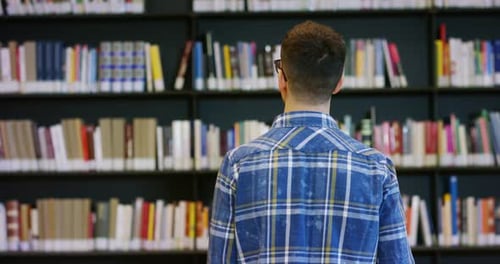 Portrait of a beautiful young man smiling happy in a library holding books after doing a search an