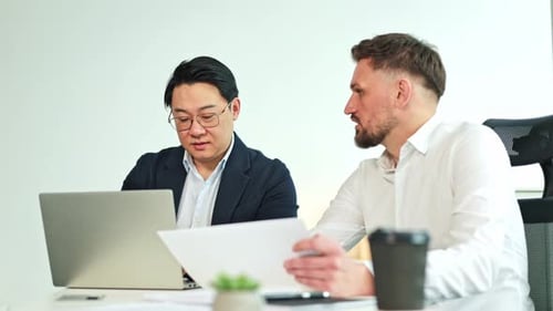 Businessmen Having a Meeting in an Office Discussing Paperwork and Laptop Content