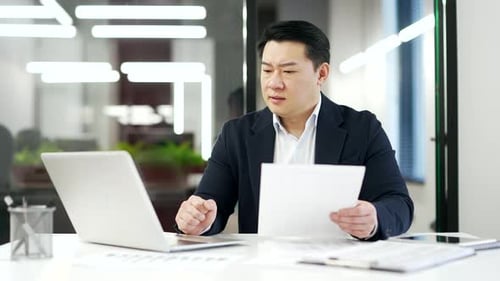 Frustrated asian financier unhappy with financial results sitting in business office. Upset puzzled