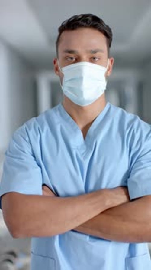 Vertical video of portrait of latino male doctor wearing face mask, slow motion