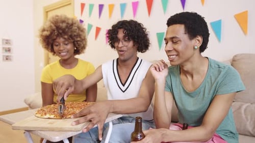 Amigos LGBTQIA cortando pizza juntos en una fiesta en casa