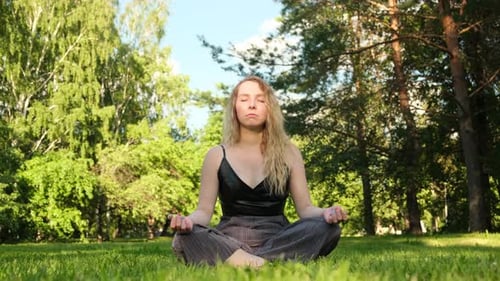Young beautiful relaxed blonde woman sitting on green grass and meditating. Concept.