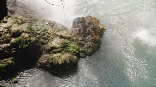 A large stone sticks out of the river. Shadows play on the water. Waterfall, view from above. Close-