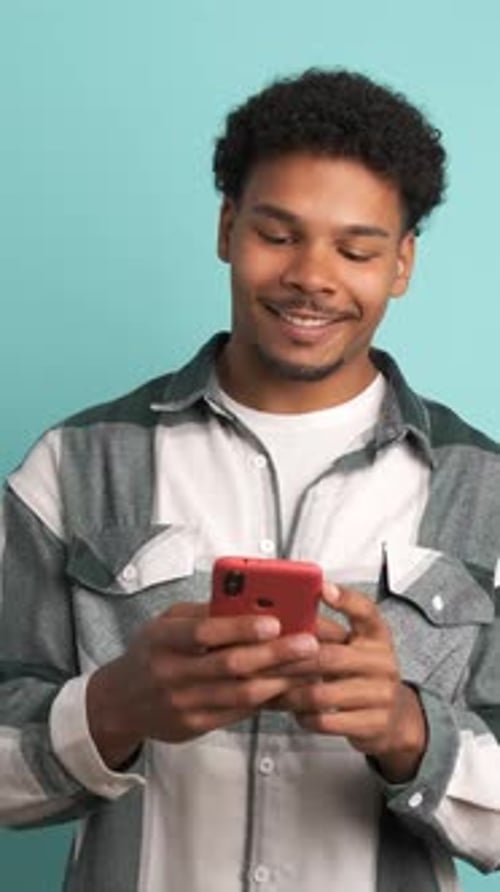 Cheerful Young Man Using Smartphone in Blue Studio