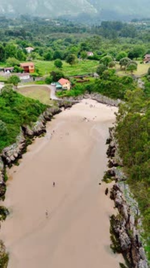 People strolling by the sandy beach among the rocks covered with greenery