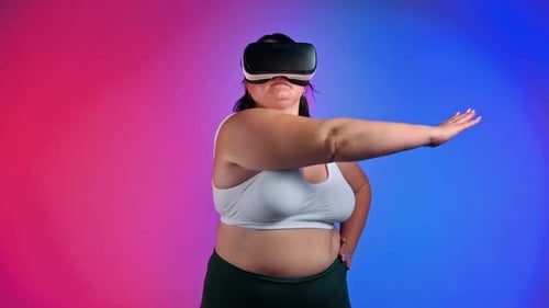 Woman with overweight in a tracksuit and VR headset doing exercises in a studio with blue and red ba