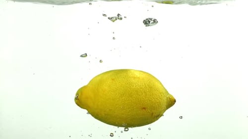 Lemon Dropping into Water with Bubbles Ascending