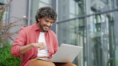 Satisfied happy young businessman received great news on laptop while sitting on a bench on street