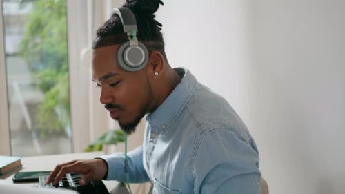 Young Adult Plays Keyboard with Headphones At Home