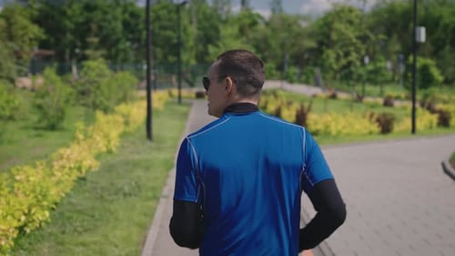 View From the Back A Man in Sportswear Runs Through a Landscaped City Park Public Urban Spaces for