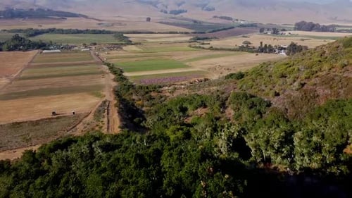 Drone shot over hill with farm and hills in the background.