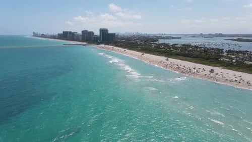 This aerial video showcases a beautiful turquoise coastline with a long, sandy beach dotted with bea