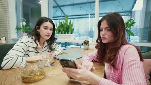 Young Women Looking at Smartphone in Cafe