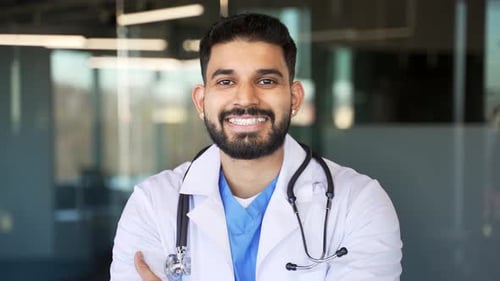 Portrait of smiling handsome doctor in white coat standing in modern hospital clinic looking