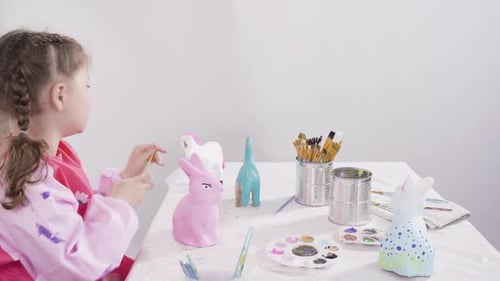 Little Girl Painting Paper Mache Figurines with Acrylic Paint for Her Homeschooling Art Project