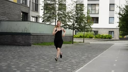 A Girl Jogging Against the Background of a Residential Area Slow Motion Girl in Black Clothes